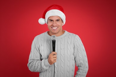 Photo of Happy man in Santa Claus hat singing with microphone on red background. Christmas music