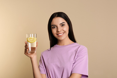 Photo of Beautiful young woman with tasty lemon water on beige background