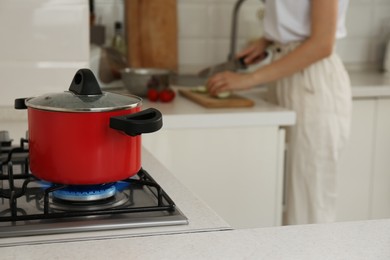 Photo of Woman cooking food in kitchen, focus on gas stove with red pot