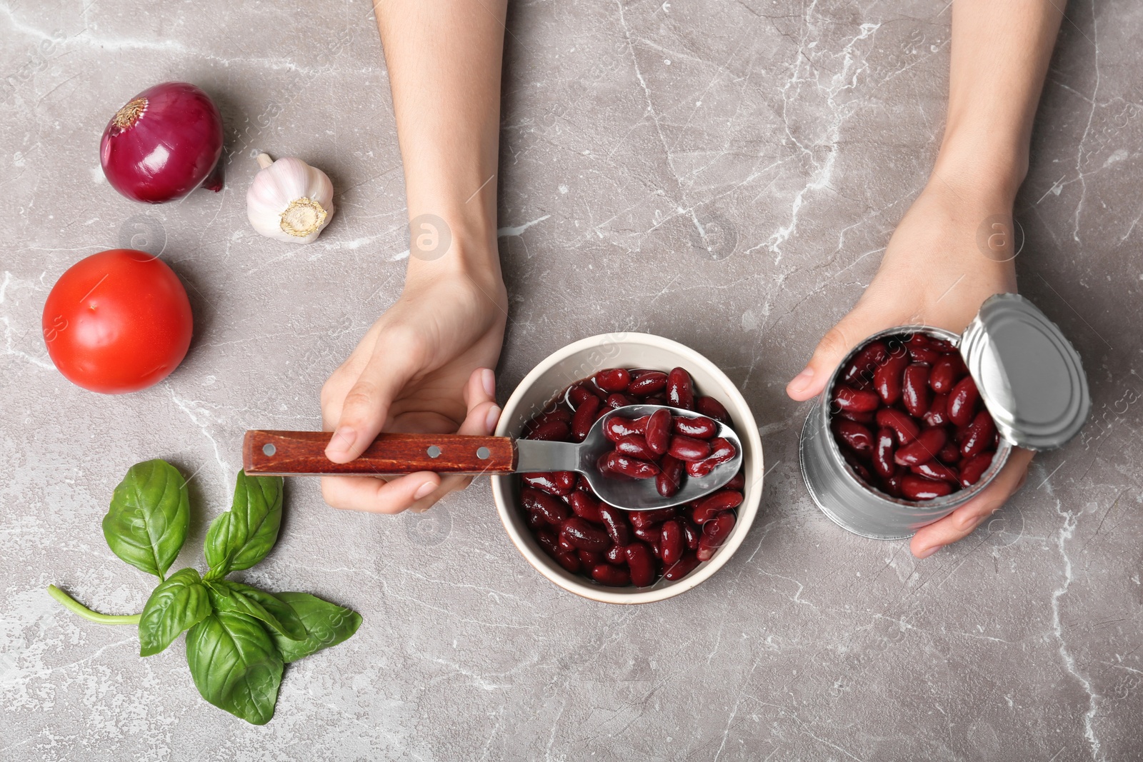 Photo of Woman with tin can of conserved beans at table, top view