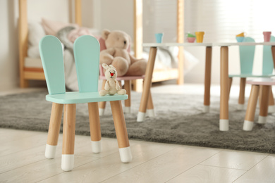 Photo of Cute chair with bunny ears and toy in children's bedroom interior