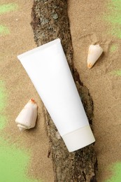 Photo of Flat lay composition with tube of cream and shells on sand against green background. Cosmetic product