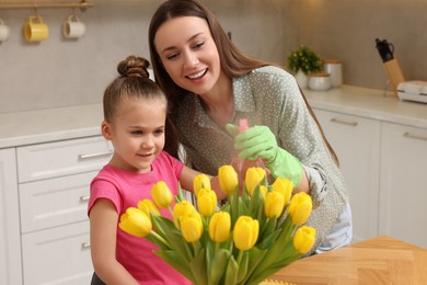 Photo of Spring cleaning. Mother and daughter spraying beautiful bouquet of yellow tulips with water at home