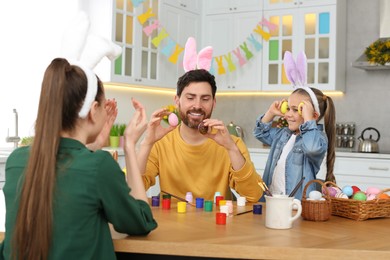 Photo of Family having fun while painting Easter eggs at table in kitchen