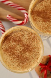 Photo of Tasty eggnog with cinnamon, cookies and candy canes on white table, flat lay