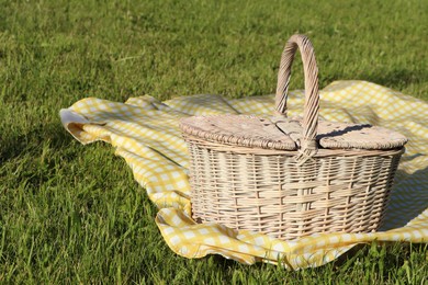 Photo of Picnic basket with checkered tablecloth on green grass outdoors, space for text