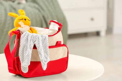 Photo of Mother's bag with baby's stuff on white table indoors. Space for text
