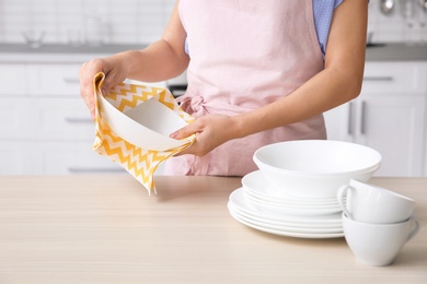 Photo of Woman wiping clean dish at table in kitchen, closeup