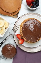 Photo of Tasty pancakes with chocolate paste, berries and fork on white marble table, flat lay