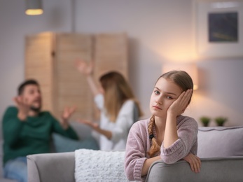 Photo of Little unhappy girl sitting in armchair while parents arguing at home