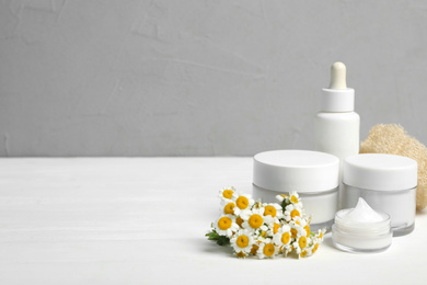 Photo of Set of cosmetic products, chamomiles and loofah on white table against grey background. Space for text
