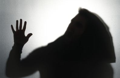 Photo of Silhouette of ghost behind glass against light grey background