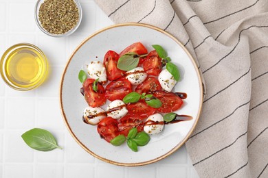 Tasty salad Caprese with mozarella balls, tomatoes, basil and other ingredients on white tiled table, flat lay