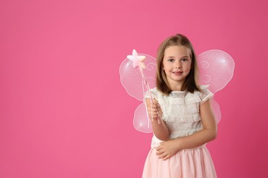 Photo of Cute little girl in fairy costume with wings and magic wand on pink background. Space for text