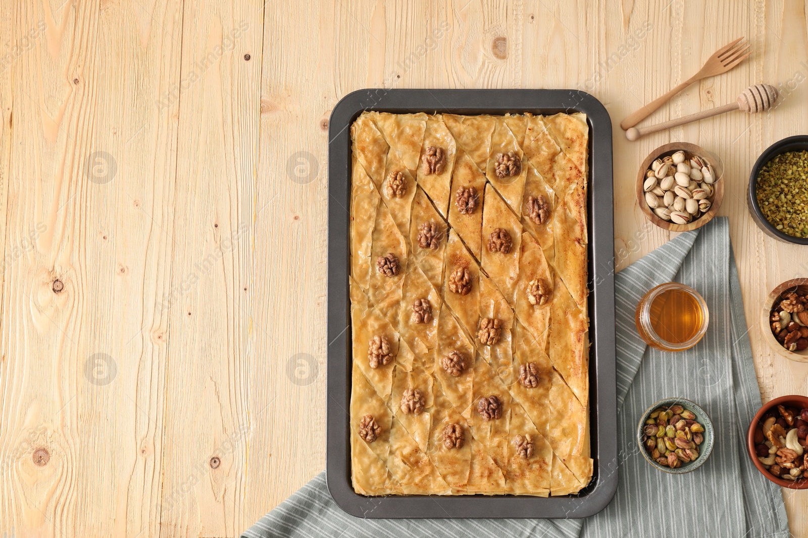 Photo of Delicious baklava with walnuts in baking pan, honey and nuts on wooden table, flat lay. Space for text