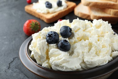 Photo of Tasty cream cheese and fresh berries on black table, closeup