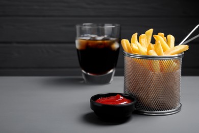 Photo of Tasty French fries, soda and ketchup on grey wooden table. Space for text