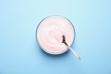 Photo of Glass bowl with creamy yogurt and spoon on color background, top view