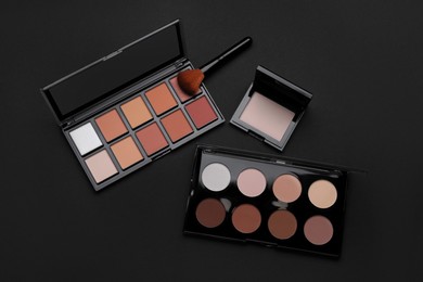 Photo of Different contouring palettes and brush on black background, flat lay. Professional cosmetic product