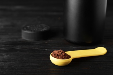 Photo of Spoon of chocolate protein powder on black wooden table, space for text