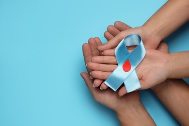 Photo of People holding light blue ribbon with paper blood drop on color background, top view and space for text. Diabetes awareness