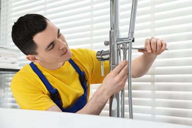Photo of Young plumber repairing faucet with spanner in bathroom
