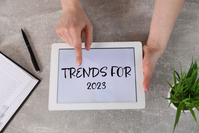 Image of Trends For 2023 text on tablet display. Woman using device at grey table, top view