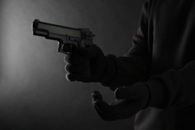 Photo of Dangerous criminal with gun on black background, closeup. Armed robbery