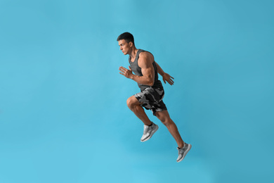 Photo of Athletic young man running on light blue background, side view
