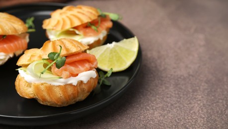 Photo of Delicious profiteroles with cream cheese, salmon and cucumber on textured table, closeup. Space for text