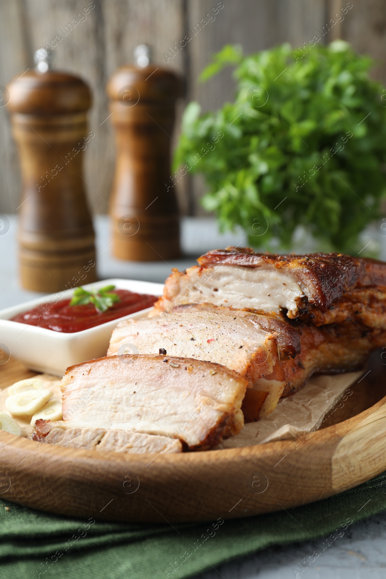 Photo of Pieces of baked pork belly served with sauce on grey wooden table