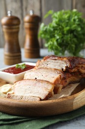Photo of Pieces of baked pork belly served with sauce on grey wooden table