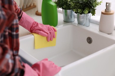 Photo of Woman cleaning kitchen sink with microfiber cloth at home, closeup