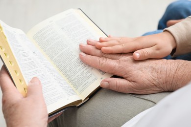 Photo of Boy and his godparent reading Bible together indoors, closeup