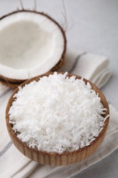 Photo of Coconut flakes in bowl and nut on light grey table
