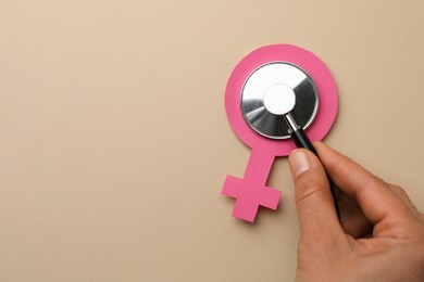 Photo of Doctor holding stethoscope near female gender sign on beige background, top view with space for text. Women's health concept