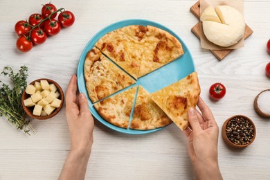 Photo of Top view of woman taking delicious khachapuri piece with cheese at white wooden table