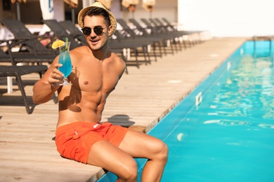 Photo of Young man with cocktail near pool on sunny day