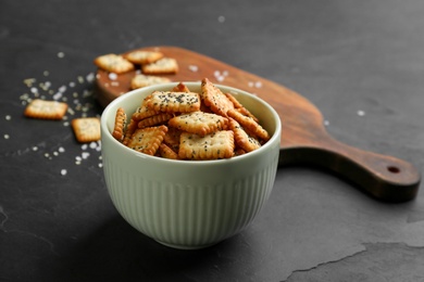 Photo of Delicious crispy crackers in bowl on black table