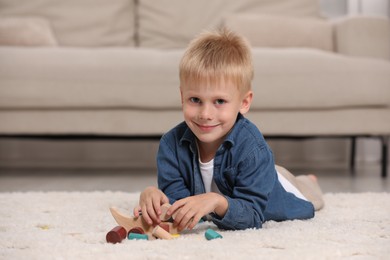 Photo of Cute little boy playing with wooden balance toy on carpet indoors