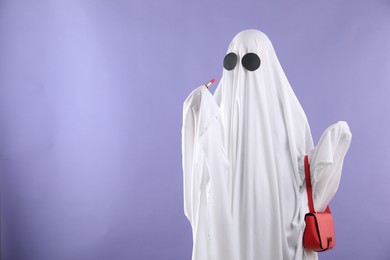 Photo of Glamorous ghost. Woman in white sheet with stylish bag and lipstick on violet background, space for text