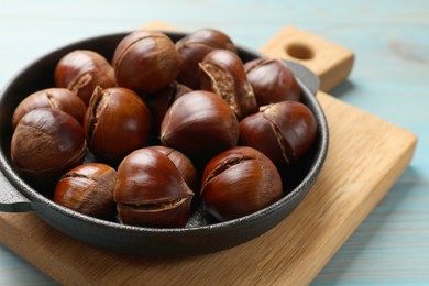 Photo of Fresh edible sweet chestnuts in frying pan on light blue wooden table, closeup