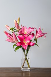 Photo of Beautiful pink lily flowers in vase on wooden table against light grey background