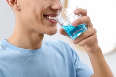 Photo of Young man using mouthwash indoors, closeup view