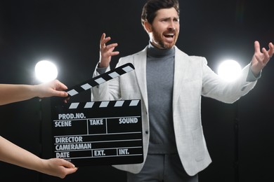Photo of Emotional actor performing while second assistant camera holding clapperboard on black background, closeup