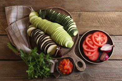 Photo of Different cut vegetables, parsley and dressing for ratatouille on wooden table, flat lay