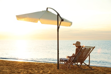 Photo of Woman with cocktail relaxing on deck chair at sandy beach. Summer vacation