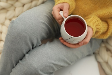 Photo of Woman with cup of tea sitting near plaid, closeup