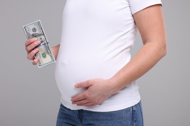 Photo of Surrogate mother. Pregnant woman with dollar banknotes on light grey background, closeup