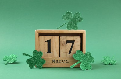 Photo of St. Patrick's day - 17th of March. Block calendar and decorative clover leaves on green background